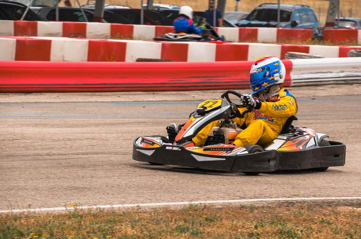Pilote de kart en action sur circuit, barrières rouges et blanches, casque coloré, tenue de course