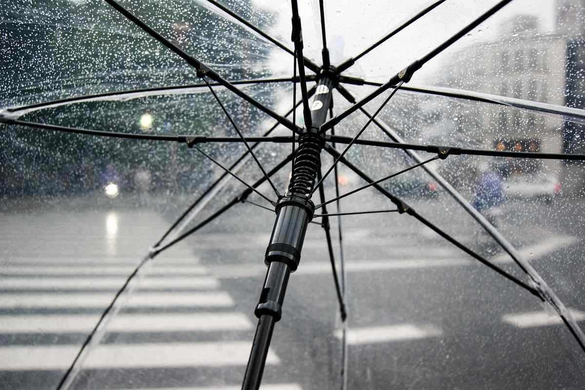 Vue d'un trottoir sous la pluie avec une personne sous un parapluie transparent