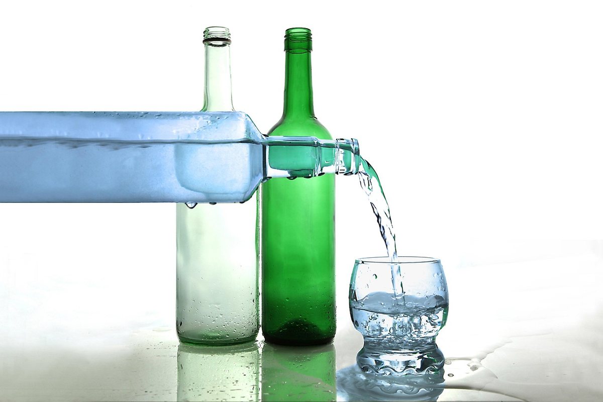 Une bouteille bleue verse de l'eau dans un verre sur un fond blanc Une bouteille bleue verse de l'eau dans un verre sur un fond blanc