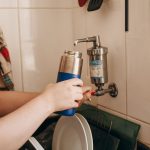 Une personne remplit une thermos bleue sous un robinet filtrant