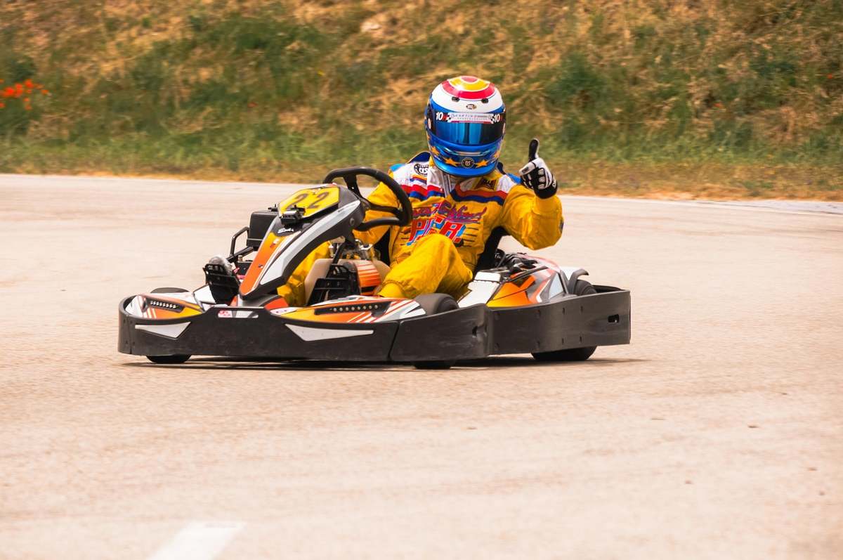 Un pilote de karting en tenue jaune sur circuit, faisant un signe