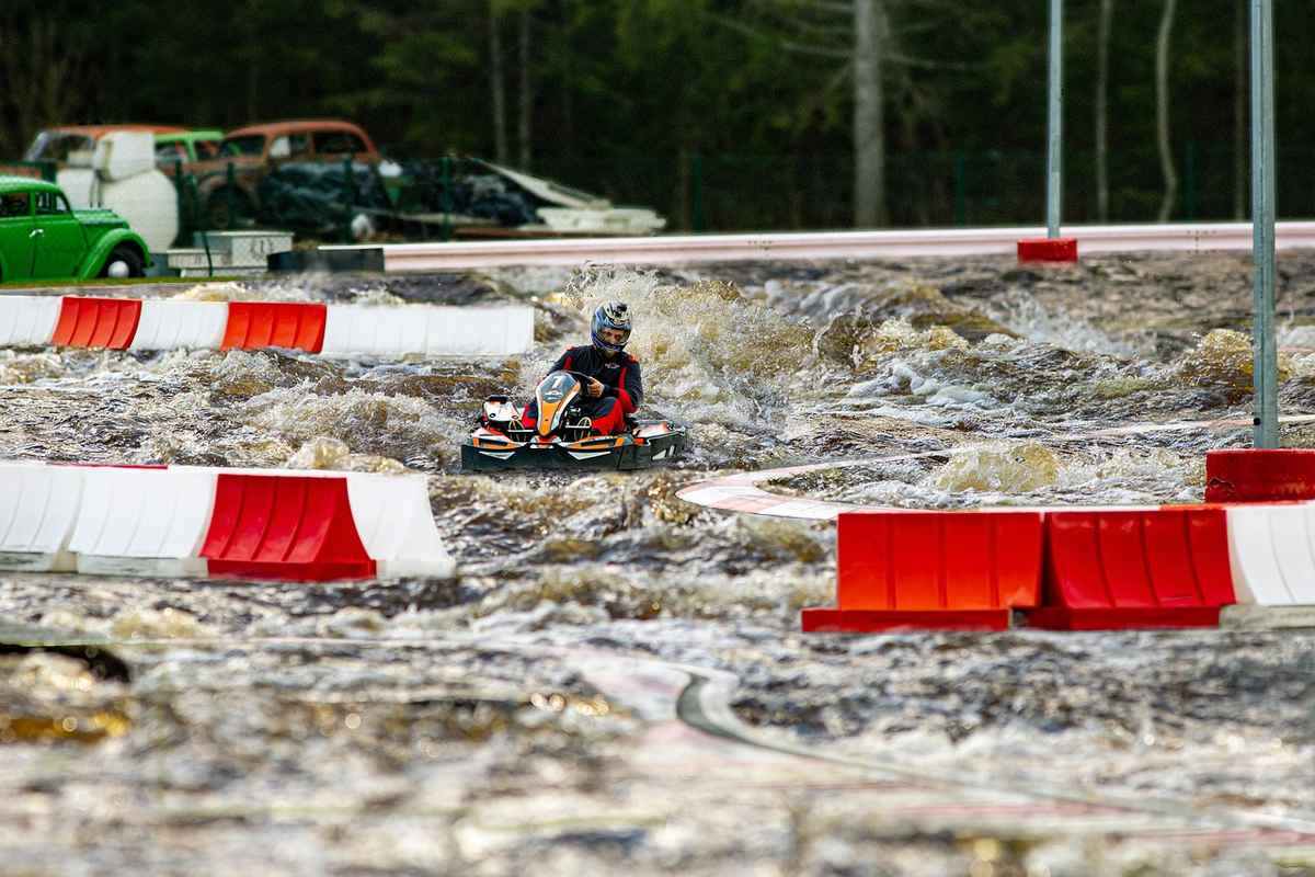 Un conducteur pilote un kart sur un circuit boueux avec barrières rouges et blanches Un conducteur pilote un kart sur un circuit boueux avec barrières rouges et blanches