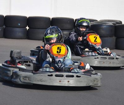 Deux enfants en karting sur une piste avec des pneus en arrière-plan