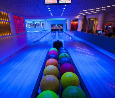 Allée de bowling éclairée, balles colorées alignées, pistes et pins visibles