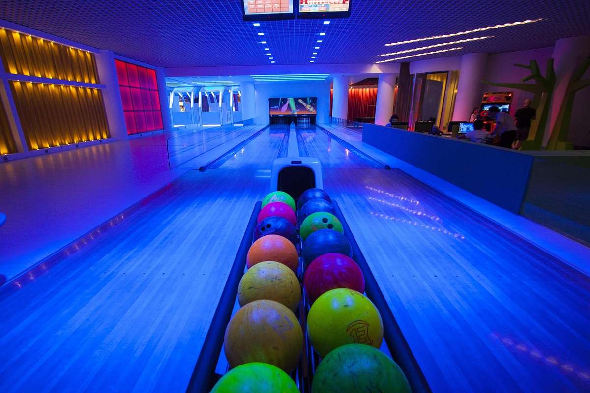 Allée de bowling éclairée, balles colorées alignées, pistes et pins visibles